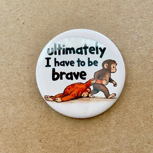 May include: A white button with the text "Ultimately I have to be brave." The button features a cartoon illustration of a brown monkey pulling an orange monkey. The orange monkey is lying on the ground.