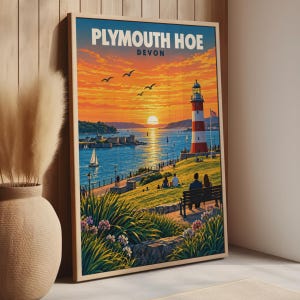 May include: A framed travel poster featuring a sunset view of Plymouth Hoe, Devon. The artwork displays a red and white lighthouse, a harbor with sailboats, and people sitting on a bench overlooking the water under a vibrant orange sky.