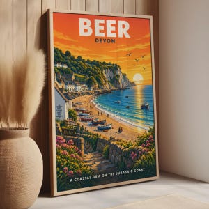Puede incluir: Un póster de viaje enmarcado titulado BEER DEVON que muestra una escena costera con una puesta de sol sobre el océano, acantilados, un pueblo con edificios blancos, botes en la arena y flores rosas, con el texto A COASTAL GEM ON THE JURASSIC COAST.