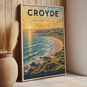 Może przedstawiać: Oprawiony plakat podróżniczy przedstawiający zachód słońca nad Croyde w North Devon w Anglii. Tekst brzmi CROYDE, NORTH DEVON, ENGLAND, SURF. SAND. SALT AIR. oraz WILD COAST. GREAT WAVES. BRIGHTER DAYS. Obraz przedstawia krajobraz wybrzeża z falami.
