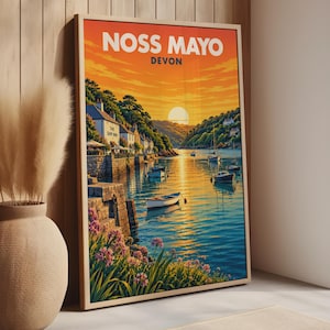 May include: A framed travel poster print titled NOSS MAYO DEVON featuring a sunset over a harbour with small boats, stone buildings including The Ship Inn, and pink flowers in the foreground. The sky is orange and yellow with a bright sun.