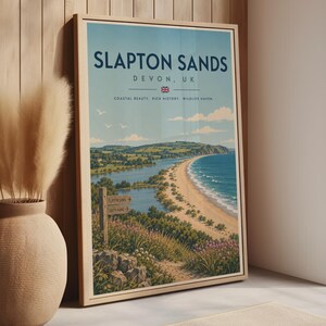 May include: A framed travel poster featuring a coastal landscape of Slapton Sands, Devon, UK. The print displays a sandy beach, blue ocean, green hills, and a wooden signpost. Text reads: SLAPTON SANDS, DEVON, UK, COASTAL BEAUTY, RICH HISTORY, WILDLIFE HAVEN.