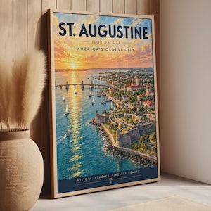 May include: A framed travel poster of St. Augustine, Florida, featuring a sunset over the water, a bridge, sailboats, and a historic stone fort. The text reads ST. AUGUSTINE, FLORIDA, USA, AMERICA'S OLDEST CITY, and HISTORY, BEACHES, TIMELESS BEAUTY.