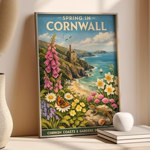 Puede incluir: Un póster de viaje vintage enmarcado titulado "Spring in Cornwall". La obra de arte representa una escena costera con un edificio, flores, una mariposa y un lagarto. El póster tiene un cielo azul y un océano.