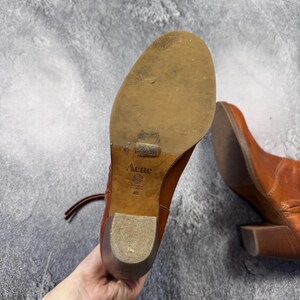 May include: A pair of brown leather ankle boots with a block heel. The soles are visible, showing the brand "Acne" and size 40. The boots have laces and a worn appearance, suggesting they are pre-owned.