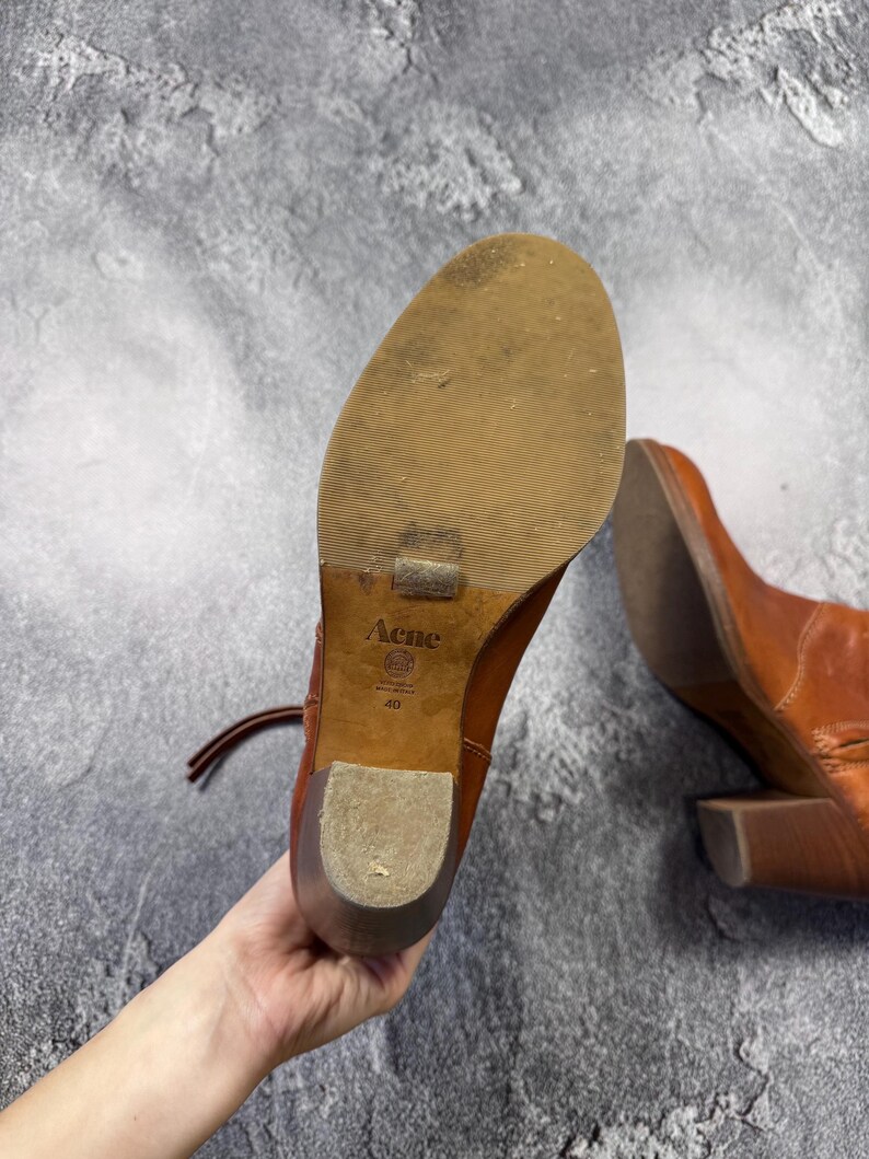 May include: A pair of brown leather ankle boots with a block heel. The soles are visible, showing the brand "Acne" and size 40. The boots have laces and a worn appearance, suggesting they are pre-owned.