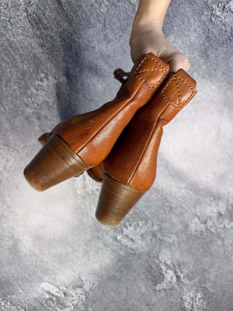May include: A pair of brown leather ankle boots with wooden heels. The boots have a classic design with a rounded toe and a stitched detail at the top of the boot. The heels are approximately 2 inches (5 cm) high.