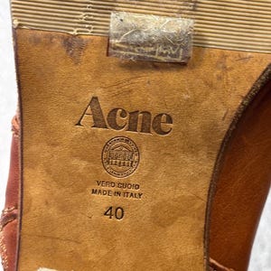 May include: Close-up of a brown leather shoe sole with the brand name "Acne" embossed. The sole also features the text "VERO CUOIO MADE IN ITALY" and the number "40".
