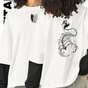 May include: White long-sleeve shirt with a black undershirt. The front of the shirt features a black and white emblem. The back of the shirt has a black and white scorpion graphic. The shirt is made of a soft material.