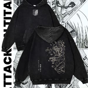 Può includere: Felpa con cappuccio nera con effetto lavato sbiadito. Presenta un emblema bianco sul petto e una grafica dettagliata sul retro. Le parole "ATTACK TITAN" sono stampate verticalmente sul lato sinistro.