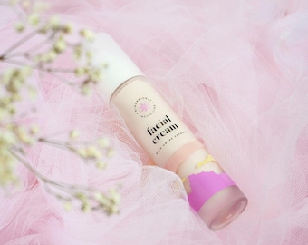 May include: A facial cream tube with a white cap and a pink and purple design. The tube is labeled "facial cream" with the words "with grape extract". The background is a soft pink tulle.