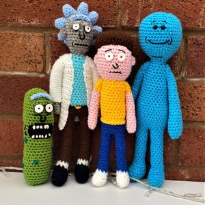 May include: Crocheted figures of characters from the animated series, Rick and Morty. The figures include Rick, Morty, Mr. Meeseeks, and Pickle Rick. Each figure is handmade with detailed features and vibrant colors, standing against a brick wall.