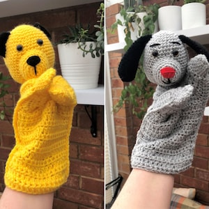 Puede incluir: Dos marionetas hechas a mano con ganchillo. Una es amarilla con orejas negras y una nariz negra. La otra es gris con orejas negras y una nariz roja. Ambas marionetas están diseñadas para colocarse sobre una mano.
