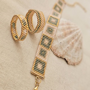 Peut inclure: Un ensemble composé de deux bagues perlées et d'un bracelet assorti, arborant un motif géométrique en perles de rocaille couleur crème, vert sauge et or métallique. Le bracelet est doté d'un fermoir doré et d'une chaînette réglable.