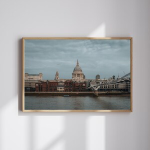 Può includere: Stampa incorniciata raffigurante il panorama di Londra, con la Cattedrale di St Paul e il Millennium Bridge, sotto un cielo nuvoloso. La cornice è in legno chiaro.