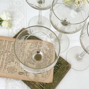 Könnte beinhalten: Ein Set aus klaren Glasstielen mit zarten, geätzten Kreuzschraffur- und Blattmustern am oberen Rand. Die Gläser haben schlanke Stiele und runde Füße, wobei die Schalen eine reflektierende Oberfläche am Boden aufweisen.