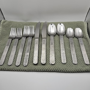 May include: A set of stainless steel flatware including four forks, two knives, two large spoons, and two small spoons. Each piece features a textured handle with a repeating geometric pattern of squares, circles, and lines along the entire length.