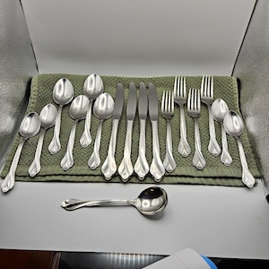 May include: A set of stainless steel flatware including various spoons, forks, and knives. The pieces feature a polished silver finish with a distinct flared, petal-like design at the base of each handle. The collection is arranged in a row.