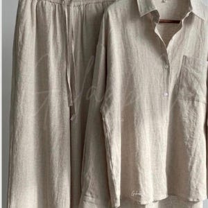Puede incluir: Un conjunto de dos piezas en color beige que consta de una camisa de manga larga con botones y bolsillo en el pecho, junto con pantalones anchos a juego que incluyen una cintura el&aacute;stica con cord&oacute;n. Las prendas son de tela texturizada clara.