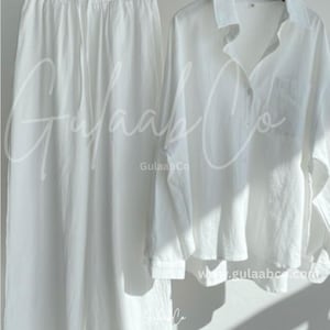 Puede incluir: Un conjunto de dos piezas blanco que consta de pantalones de pierna ancha con cintura el&aacute;stica con cord&oacute;n y una camisa de manga larga con botones y bolsillo en el pecho. El texto GulaabCo y www.gulaabco.com es visible en las prendas blancas.