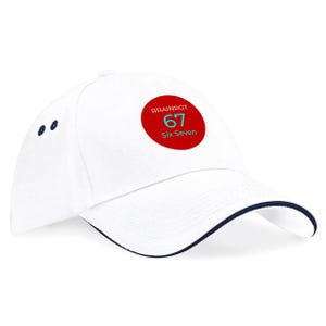 Pode incluir: Boné de beisebol branco com aba e detalhes em azul marinho. O boné apresenta um patch circular vermelho com o texto "BRAINROT 67 Six Seven" em branco e turquesa. Um acessório moderno.