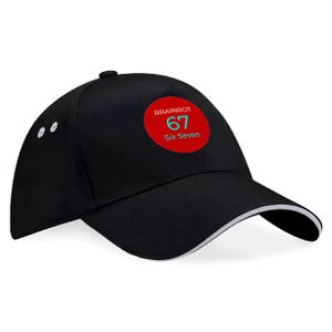 Pode incluir: Boné de beisebol preto com uma borda branca na aba. O boné apresenta um patch circular vermelho com o texto "BRAINROT 67 Six Seven" em branco e verde-azulado. O boné tem uma aba curva e um botão no topo.