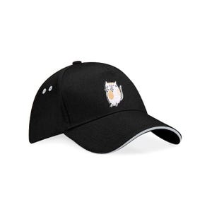 Peut inclure: Casquette de baseball noire avec une bordure blanche et un petit motif de chat brodé sur le devant. La casquette a une visière incurvée et un bouton sur le dessus. Le chat est blanc avec un ventre beige.