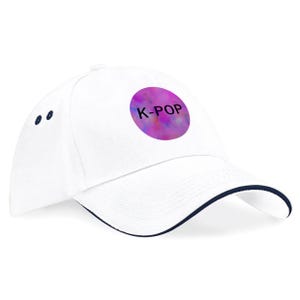 May include: White baseball cap with a navy blue brim and accents. The cap features a purple circle with the text "K-POP" in white. The design is a colorful, abstract pattern.