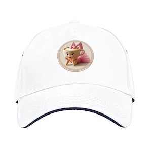 Pode incluir: Boné de beisebol branco com aba azul marinho. O boné apresenta um gráfico circular de uma xícara de café de desenho animado usando um tutu e laço rosa. A xícara de café tem um rosto sorridente e está apoiando o queixo nas mãos.