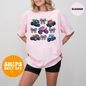 A woman wearing a pink t-shirt with a graphic of colorful monster trucks and checkered flags.