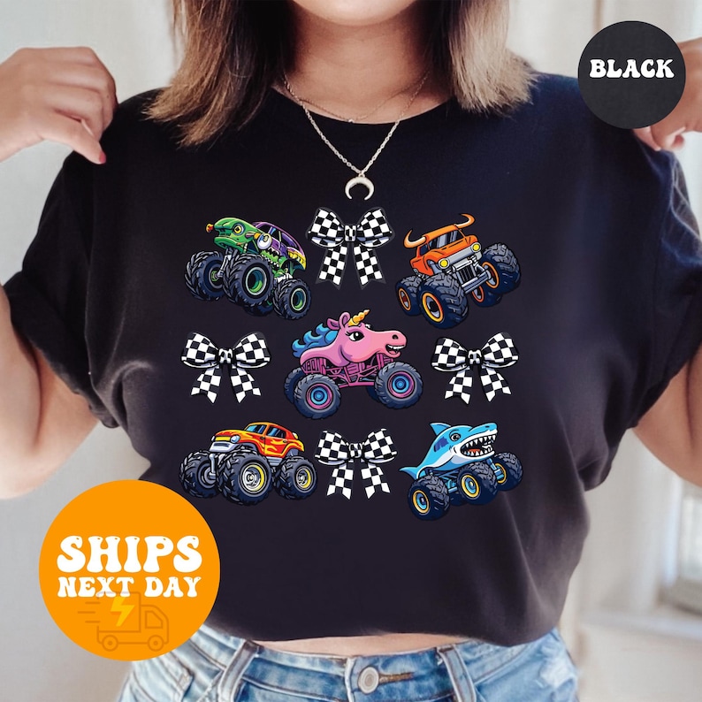 A person wearing a black t-shirt with a graphic design of colorful monster trucks and checkered flags.