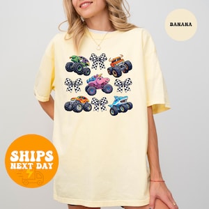 A woman wearing a yellow t-shirt with a graphic of colorful monster trucks and checkered bows.