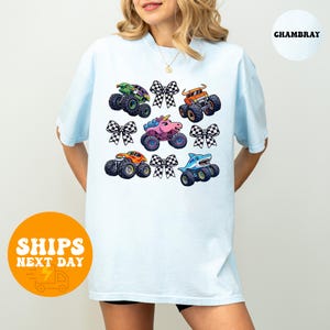 A woman wearing a white t-shirt with a graphic design of various monster trucks and checkered bows.