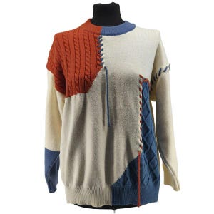 Può includere: Un maglione color block dal design unico. Il maglione presenta sezioni color crema, arancione ruggine e blu navy. La sezione arancione ruggine ha un motivo a trecce. Le cuciture sono accentate da cuciture decorative.
