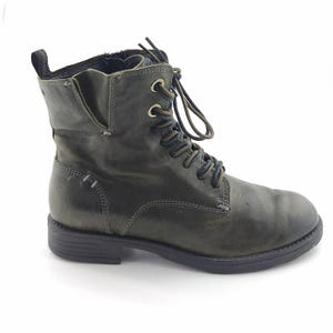 Peut inclure: Une botte en cuir vert foncé avec un laçage. La botte a un petit talon et une tirette à l'arrière. Les lacets sont marron foncé et les coutures sont visibles. La botte mesure environ 15 cm de haut.