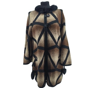 Peut inclure: Cape marron et noir à motifs avec col en fourrure noire et bordures noires. La cape présente un motif géométrique et est fermée par des fermetures en cuir. De petits pompons noirs ornent les bords inférieurs.