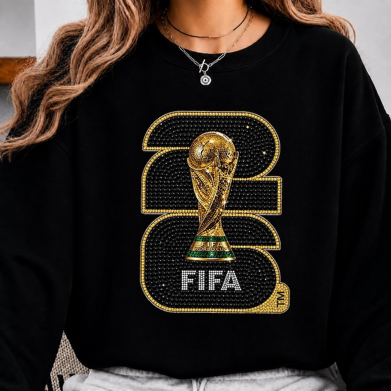 Op de afbeelding: Zwarte sweatshirt met een gouden FIFA World Cup trofee ontwerp. Het nummer "2022" is omlijnd met gouden en zwarte strass-steentjes, met het woord "FIFA" in het wit aan de onderkant. Het ontwerp is gecentreerd op de voorkant.