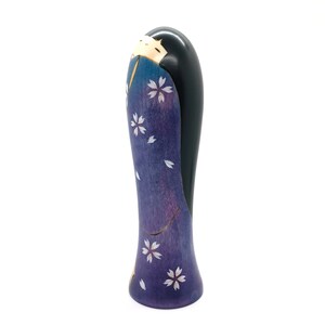 May include: A wooden figurine of a woman in a purple and blue kimono with white cherry blossoms. The figurine is hand-painted and has a black hair.