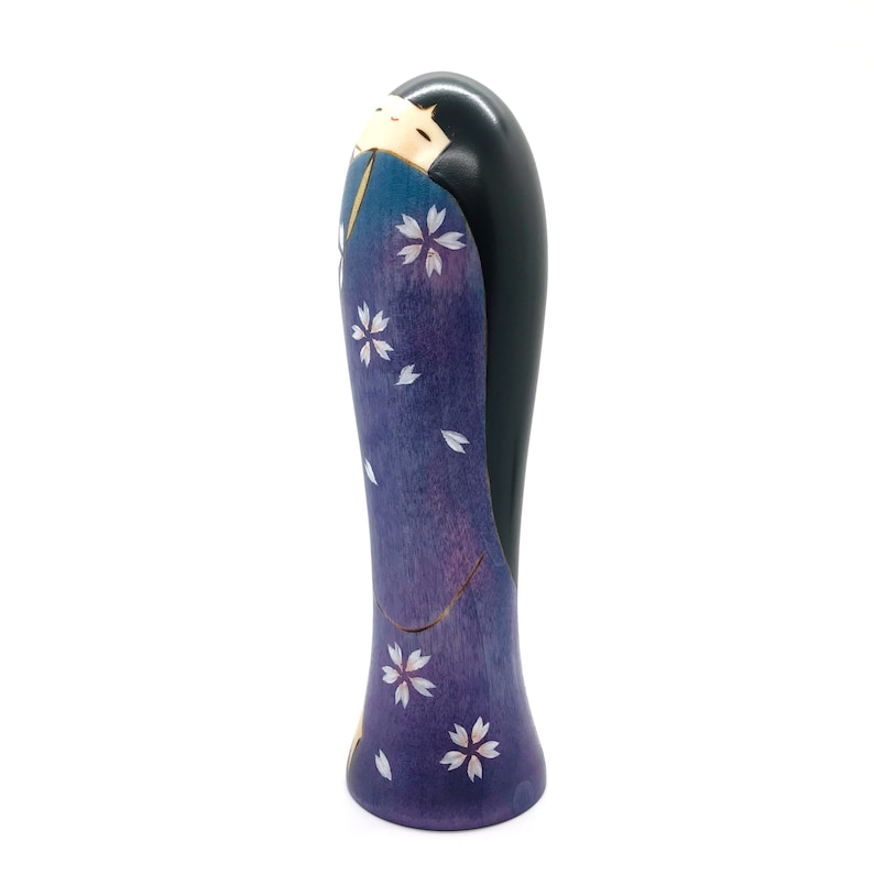 May include: A wooden figurine of a woman in a purple and blue kimono with white cherry blossoms. The figurine is hand-painted and has a black hair.