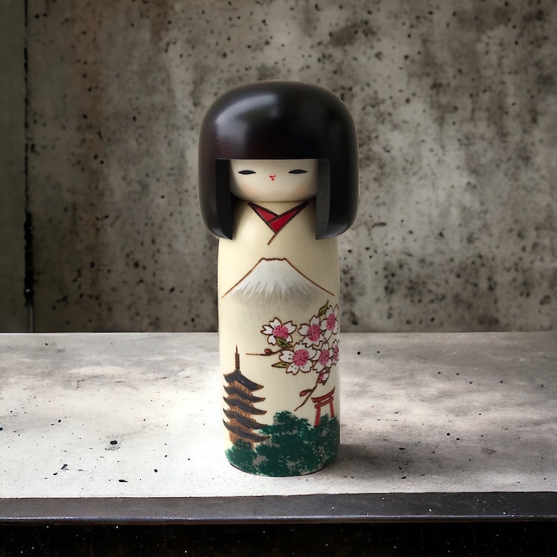 May include: A traditional Japanese kokeshi doll with black hair and a white kimono. The doll is painted with a scene of Mount Fuji, cherry blossoms, a pagoda, and a torii gate.