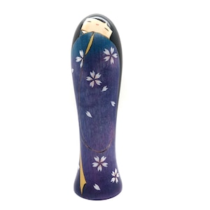 May include: A wooden doll with a purple and white floral pattern. The doll has black hair and a painted face.