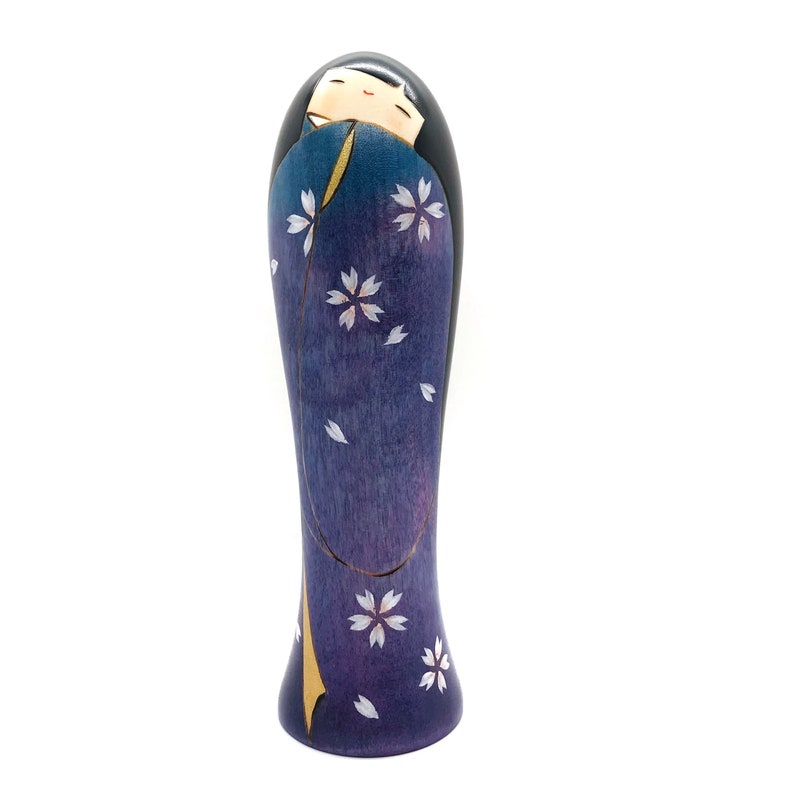 May include: A wooden doll with a purple and white floral pattern. The doll has black hair and a painted face.
