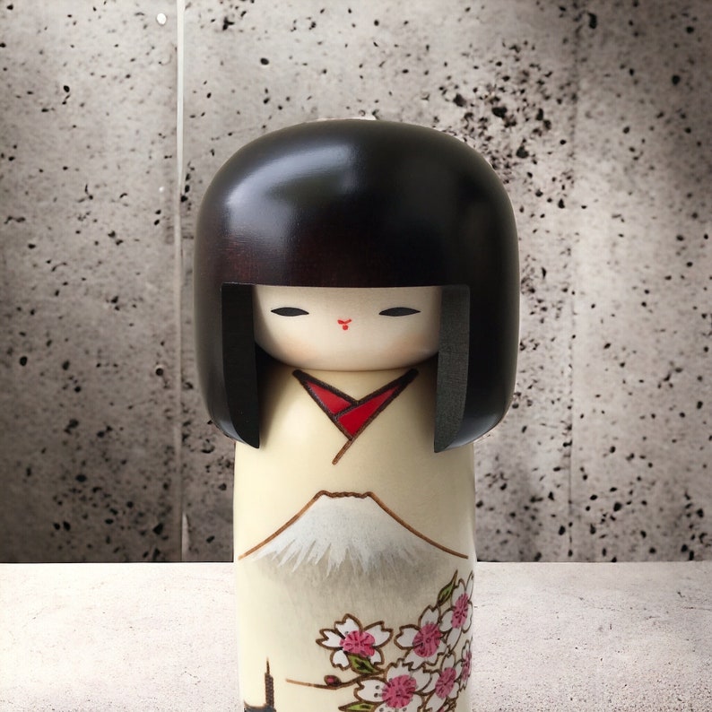 May include: A traditional Japanese kokeshi doll with black hair, a white and red kimono, and a painted design of Mount Fuji and cherry blossoms.
