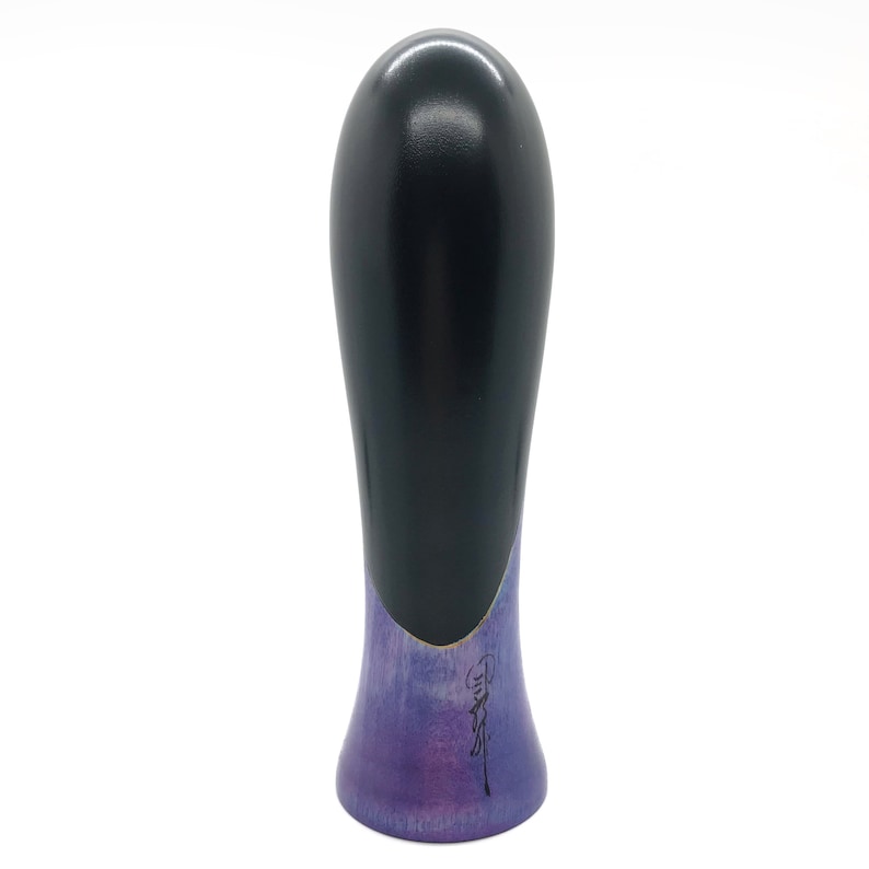May include: A black and purple wooden bottle stopper with a rounded top and a flared base. The base is painted with a purple and blue gradient and features a black signature.