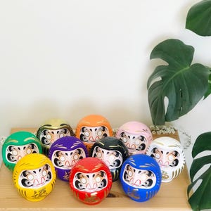 May include: A collection of ten colorful Japanese lucky cat figurines, also known as "Maneki-Neko", with gold accents. The figurines are arranged in a circle on a wooden surface.