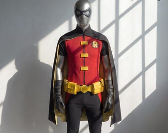 May include: A full-body costume of a superhero, featuring a red and black top with yellow accents, a black cape, and black pants. The costume includes a yellow belt and a mask. The logo "Handcrafts by UMAR" is in the upper right corner.