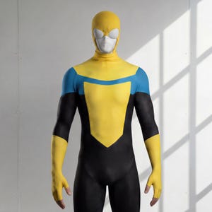 Può includere: Un costume da supereroe a corpo intero con cappuccio giallo e lenti oculari bianche, pannello pettorale giallo, accenti blu sulle spalle e maniche e gambe nere. Il tessuto presenta un sottile motivo testurizzato nelle sezioni nere del costume.