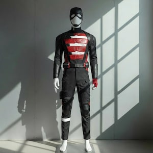 以下が含まれることがあります： マネキンの全身コスチューム。コスチュームは黒、赤、白で、黒いマスクと手袋が付いています。胸の部分は赤と白のストライプのデザインです。パンツは黒で、ポケットと膝パッドが付いています。白いストライプが脚の下部にあります。