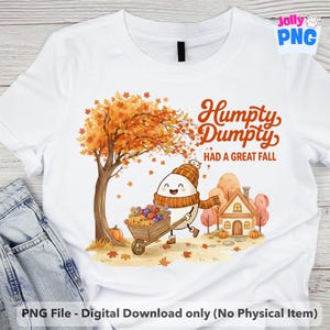 May include: White t-shirt featuring a whimsical illustration of Humpty Dumpty in a fall scene. The design includes a tree with orange leaves, a house, and Humpty Dumpty pushing a wheelbarrow of pumpkins. Text reads "Humpty Dumpty HAD A GREAT FALL".