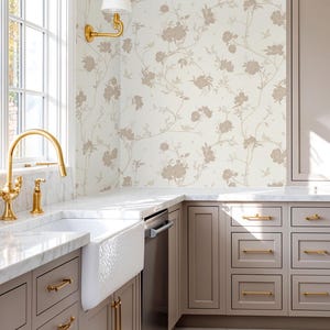 May include: A kitchen interior featuring light taupe cabinets with gold hardware, a white farmhouse sink, and a marble countertop. The wall is covered in wallpaper with a white background and a repeating pattern of light brown floral vines and birds.